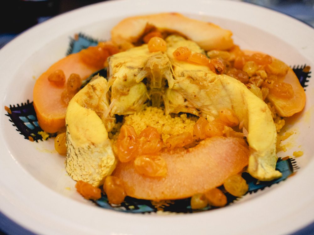 Fish with couscous, peaches and sultanas on a white and blue plate