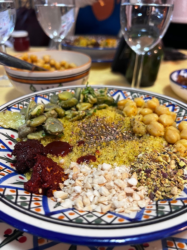 plate with couscous, chickpeas, broad beans, chopped nuts, pistasios and harissa
