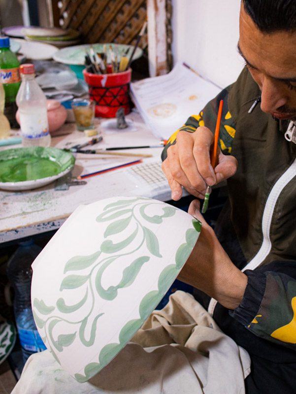 man painting a white bowl with green paint in a floral pattern
