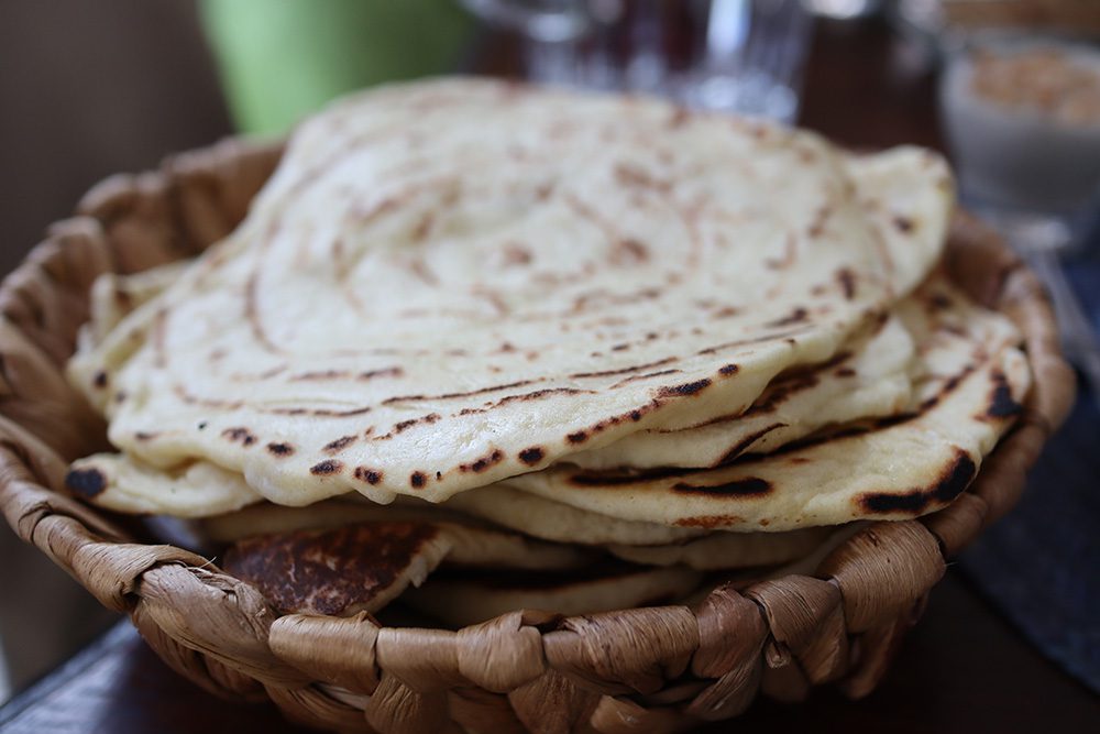 a bowl of cooked mwali, round disc of flatbreads in a wicker bowl