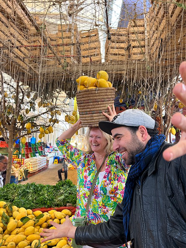 holding a basket of lemons on my head beside Hamza in the Central Market with lemons around me.
