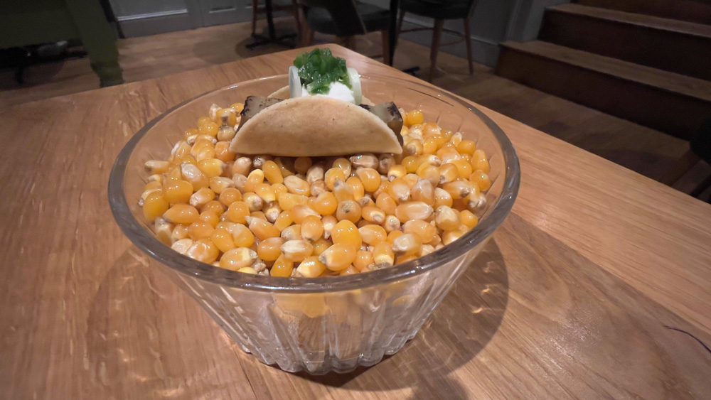 amuse bouche of charred aubergine taco on a bed of corn