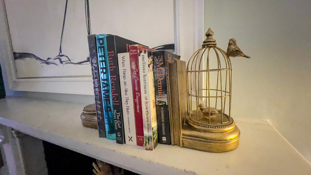 small gold birdcage with fake birds holding up 7 books on a white mantlepiece