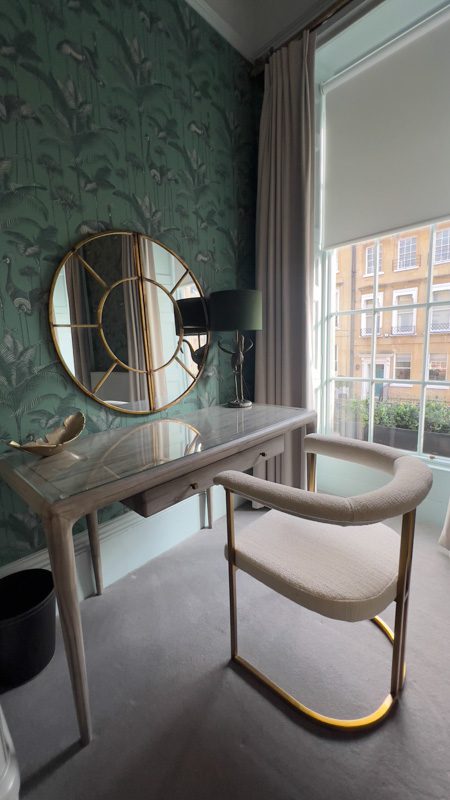 glass topped table with round mirror above bedside a window