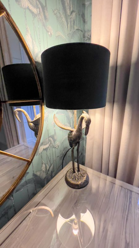 gold coloured lamp in shape of a crane bird with a green lampshade reflectong in a mirror