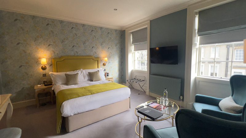Superior Room with king size bed with yellow headboard, blue walls and seats