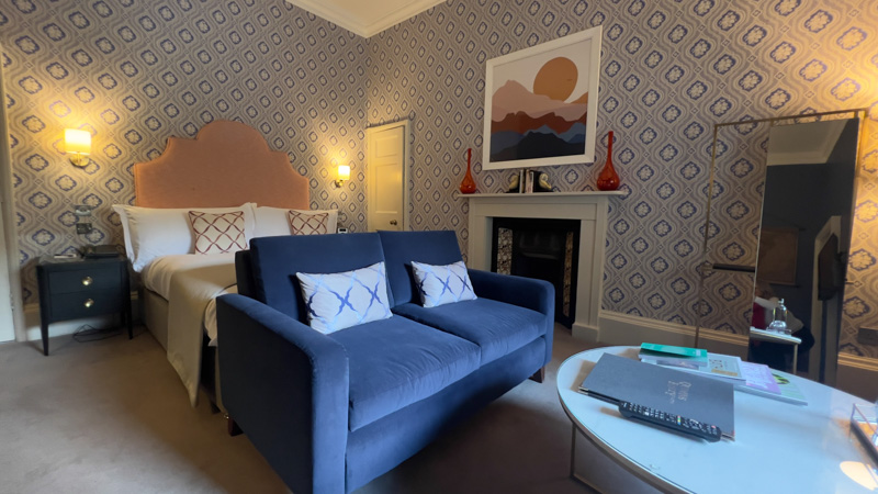 bed with apricot coloured headboard, navy blue sofa and blue and cream wallpaper