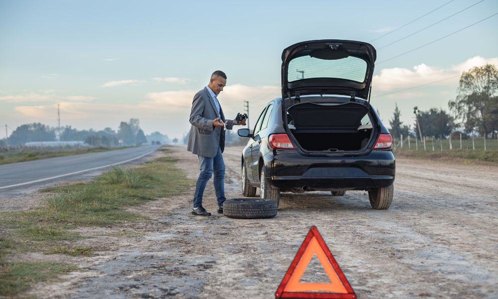 man standing beside car with spare tire and a warning triangle