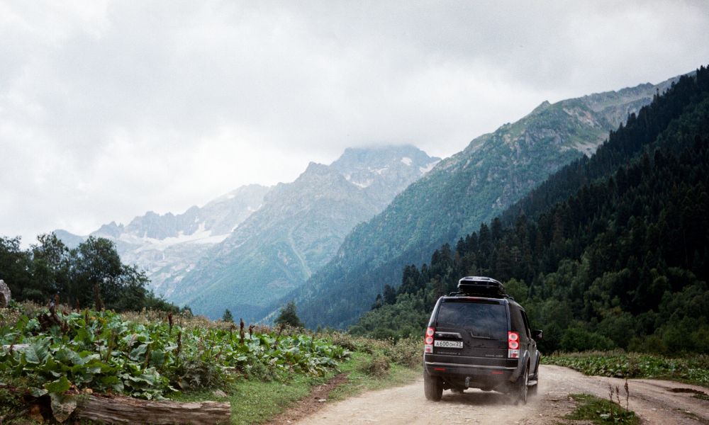 vehicle on mountain road with mountains in the background