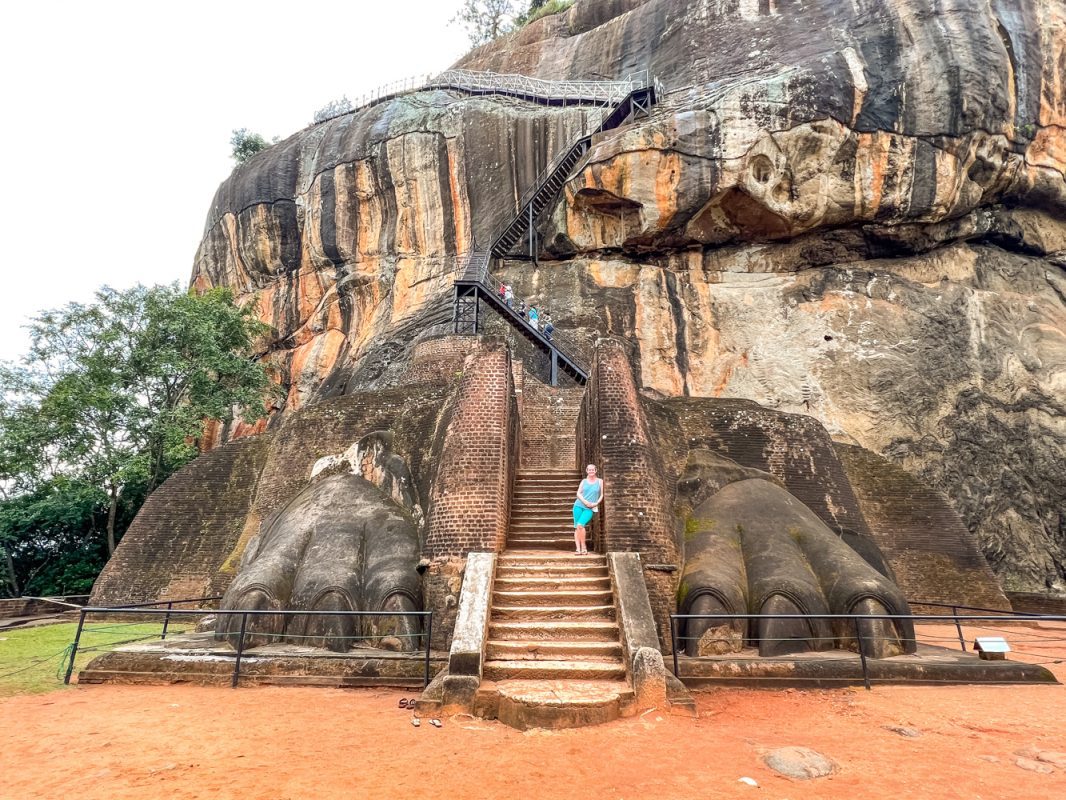Larch weating a blue t-shirt and shorts standing between the two great lion paws with the Lion Rock behind