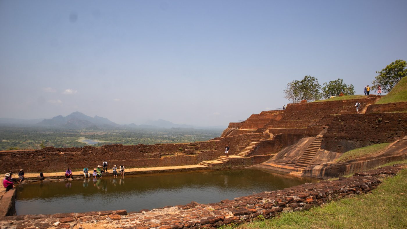 The swimming pool at the summit with people dipping their feet in with hills and jungle behind