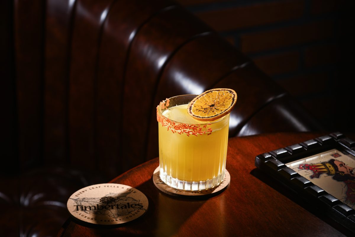Enjoy a cocktail in the Cellar Lounge - glass tumbler with a yellow cocktail with orange sprinkles round half the outside of the rim and a singed orange slice