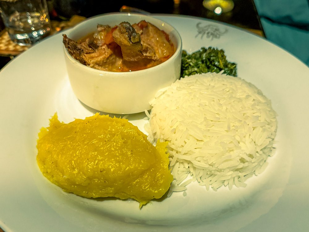 Plate of matooke and rice with meat stew and greens